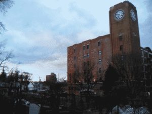 A dithered warehouse with a clock tower under and overcast sky