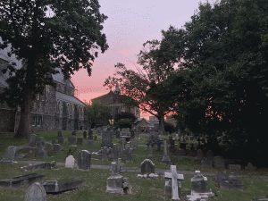 A purple and pink sunset sky over a graveyard and church with big lush trees