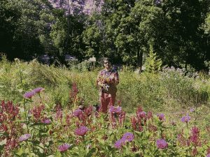 A dithered image of Travis standing in a field of flowers with trees in the background